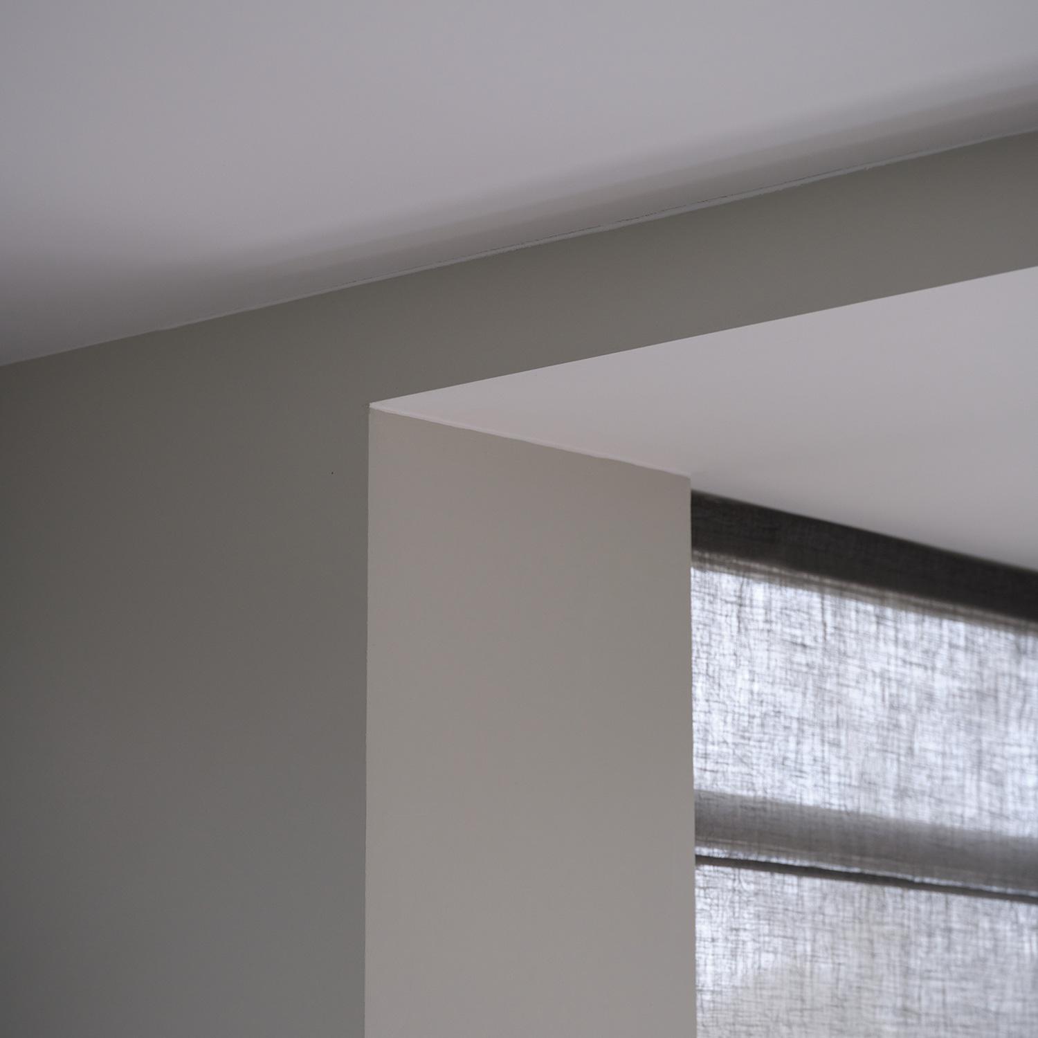 Een raam in een kamer met een witte muur en akoestisch plafond, met natuurlijk licht en een frisse uitstraling. 